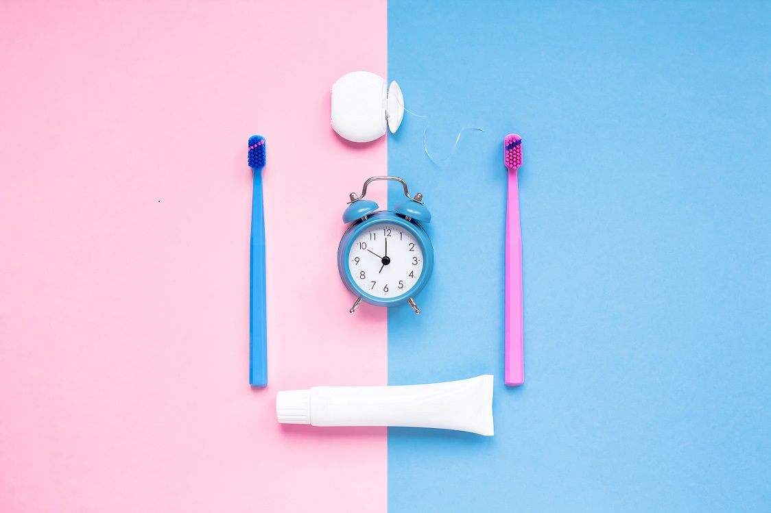 Teeth hygiene and oral dental care products and alarm clock on color pink and blue background